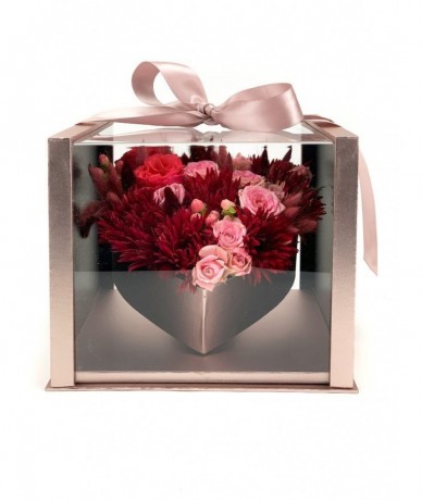 Rose-coloured box with transparent lid and a ribbon, inside a heart formed by red and pink flower heads